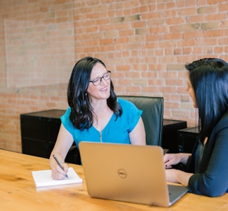 woman in teal t-shirt sitting beside woman in suit jacket