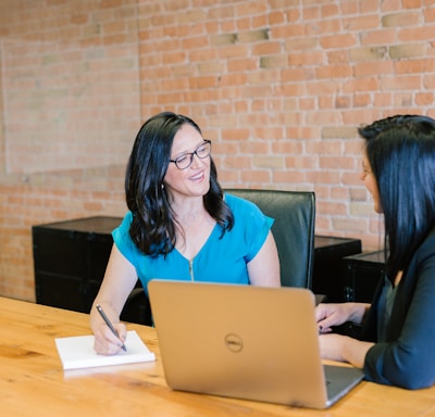 woman in teal t-shirt sitting beside woman in suit jacket