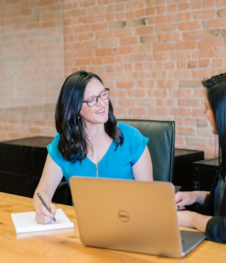 woman in teal t-shirt sitting beside woman in suit jacket