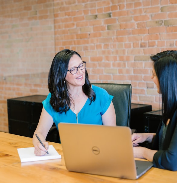 woman in teal t-shirt sitting beside woman in suit jacket