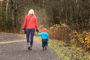 Siblings holding hands wearing matching colorful seasonal jackets in autumn leaves.