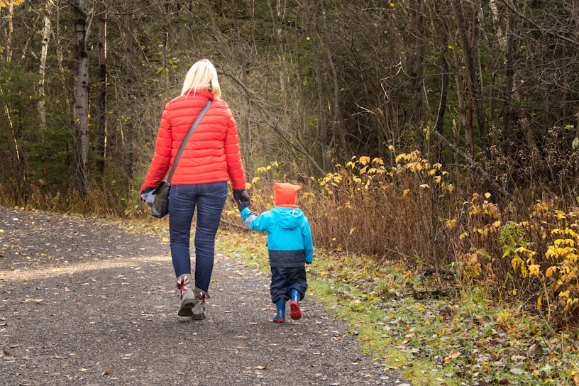 A cozy autumn afternoon scene with a mother and child wearing oversized denim jackets and soft hoodies, surrounded by golden leaves.