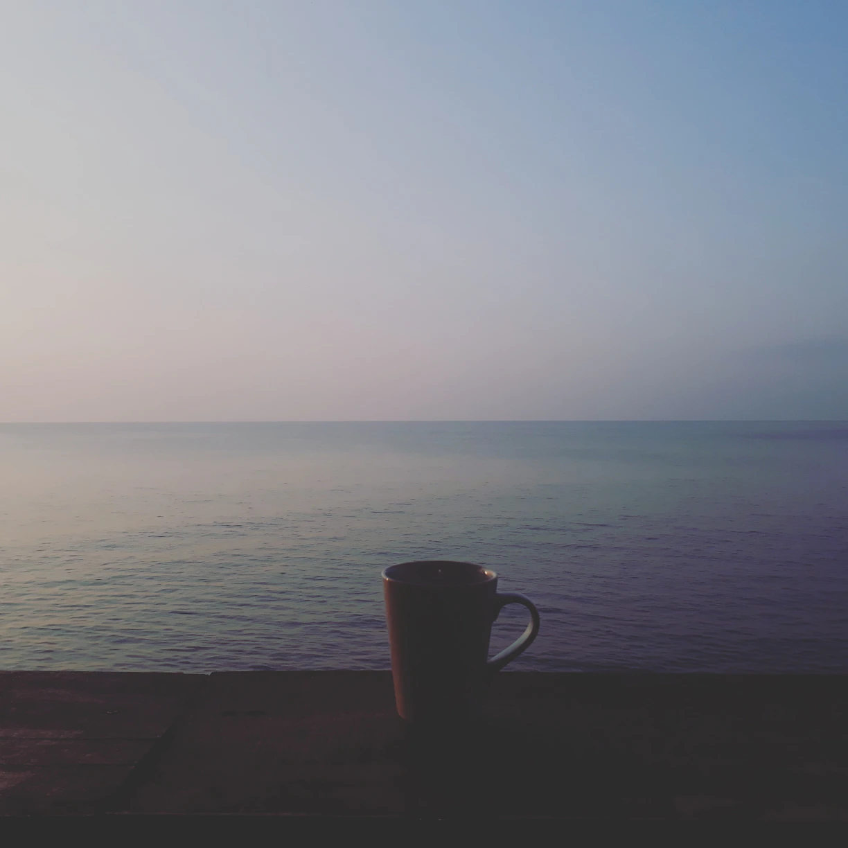 A serene morning scene with soft blue skies and a person enjoying a peaceful moment with a cup of tea.