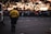 A traffic emergency patrol officer stands on a street facing a large, gathered crowd behind safety barriers. The crowd appears to be at an event or parade during sunset, with a van nearby and silhouettes of large trees in the background.