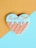 A heart-shaped cookie is decorated with a light blue icing on the top half, adorned with colorful sprinkles. The bottom half of the cookie has a waffle pattern in light brown. The background features a diagonal split between mustard yellow and pastel blue colors.