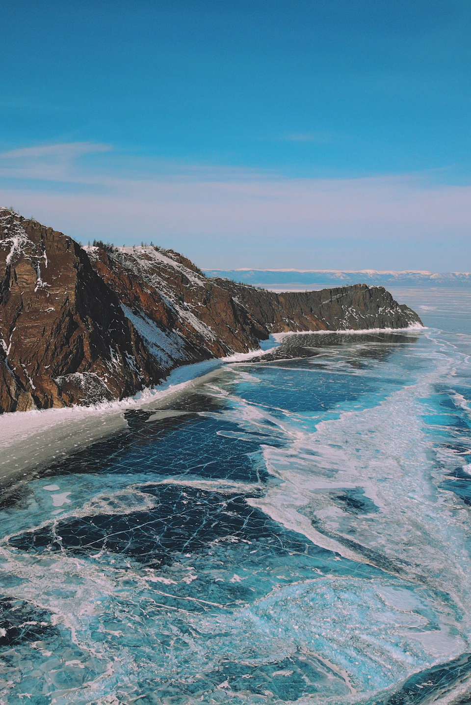 Frozen lake on rocky coastline with clear blue sky above in winter landscape