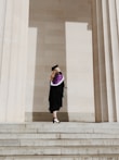 woman in academic regalia standing near concrete stairs