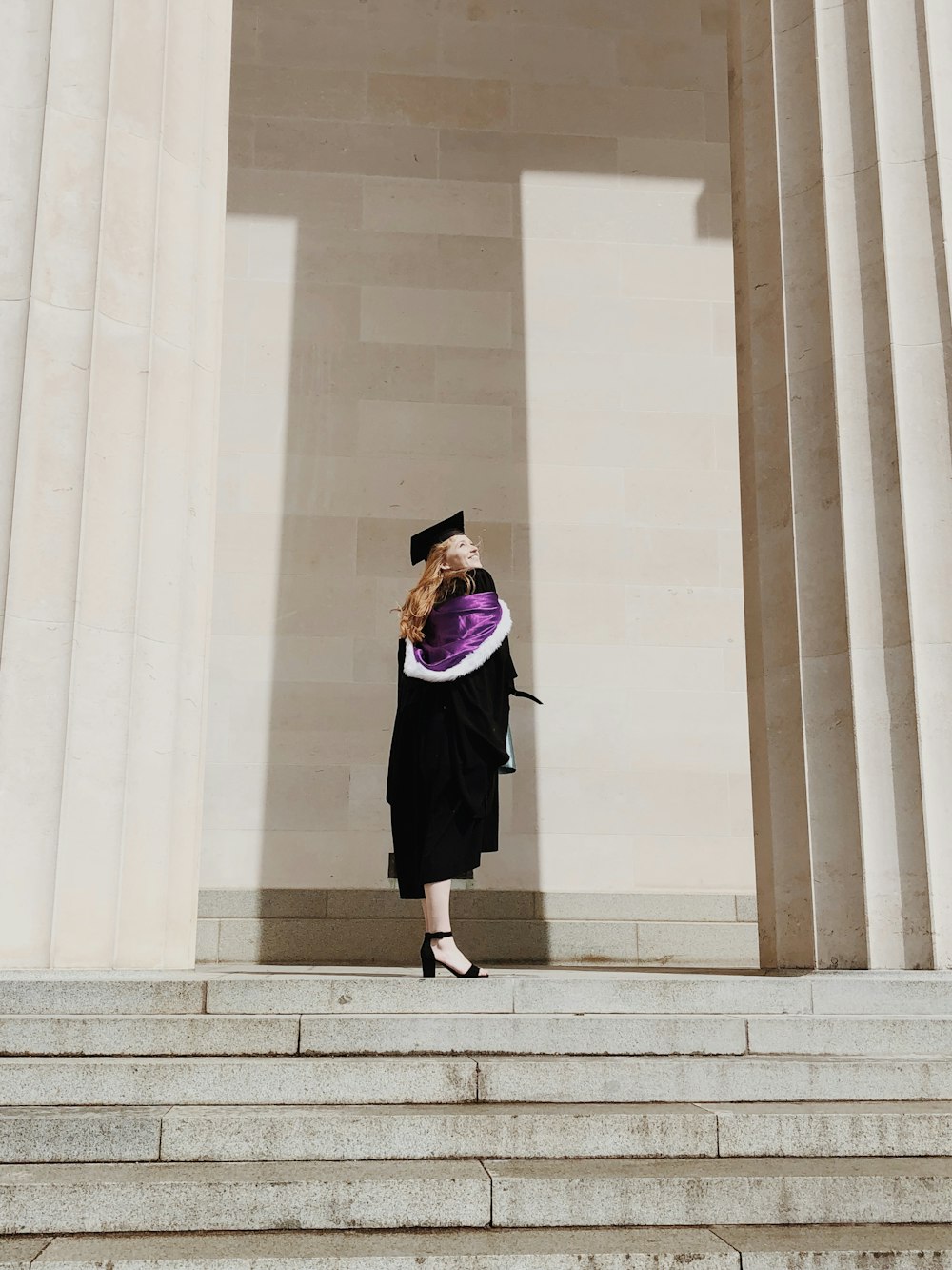 woman in academic regalia standing near concrete stairs