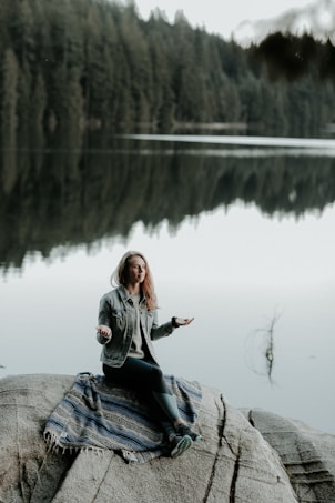 woman meditating on rock in bank of lake