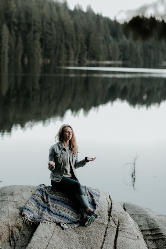 woman meditating on rock in bank of lake
