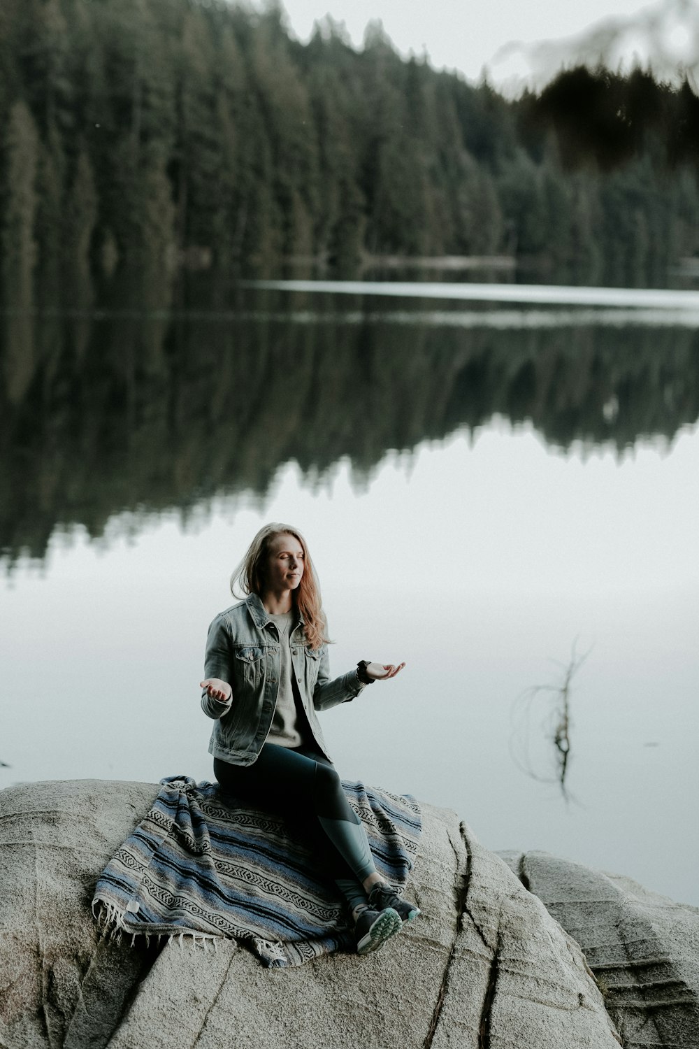 Frau meditiert auf Felsen am Ufer des Sees