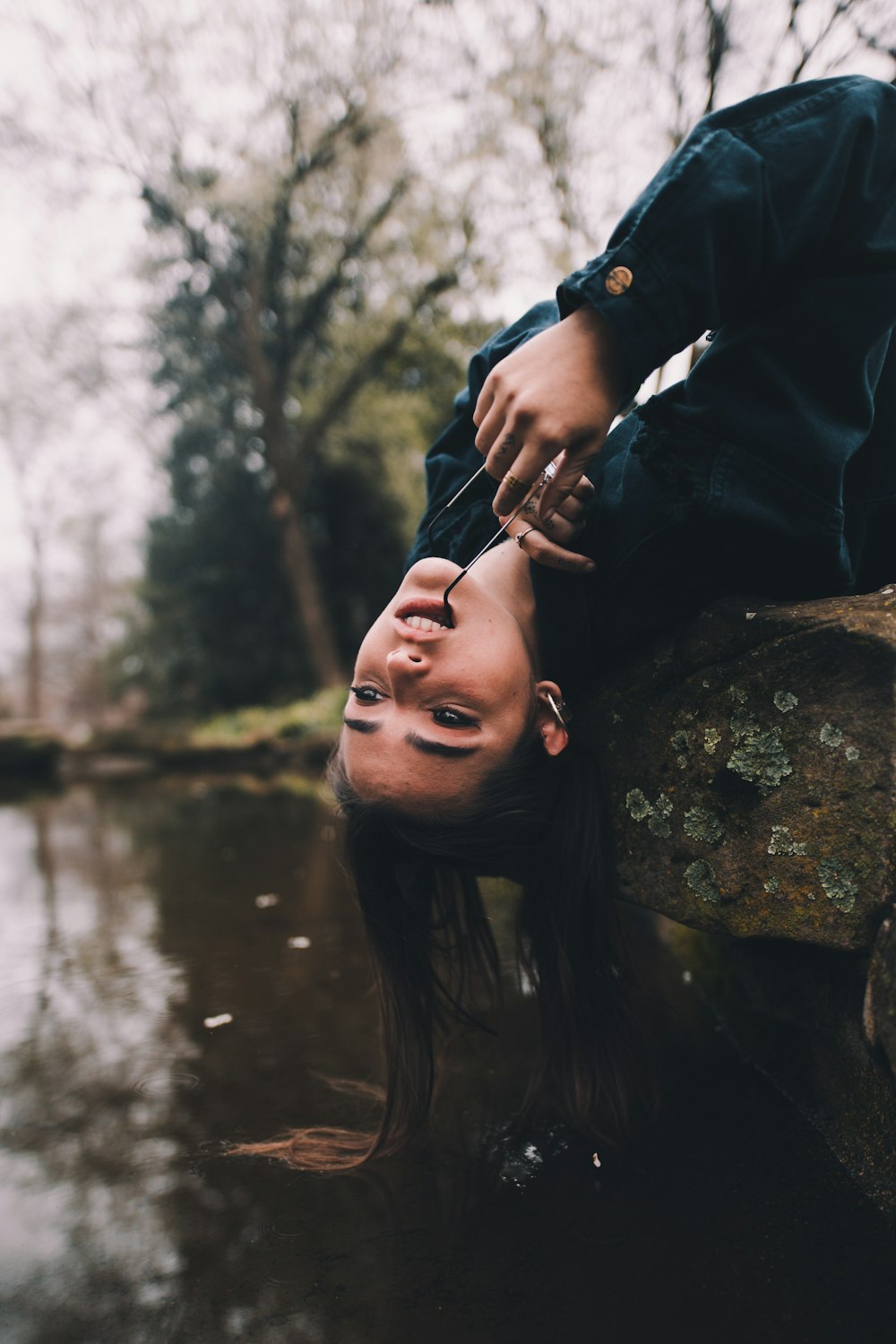 selective focus photography of woman sitting on moss-covered stone with hair on river during daytime