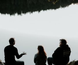 silhouette of three people sitting on cliff under foggy weather