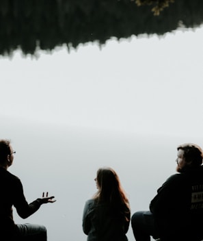 silhouette of three people sitting on cliff under foggy weather