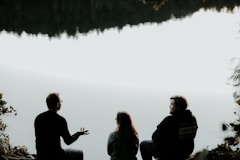 silhouette of three people sitting on cliff under foggy weather