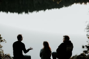 silhouette of three people sitting on cliff under foggy weather