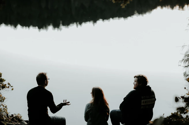 silhouette of three people sitting on cliff under foggy weather