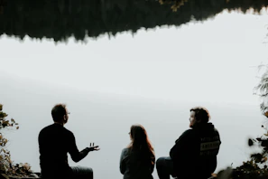 silhouette of three people sitting on cliff under foggy weather
