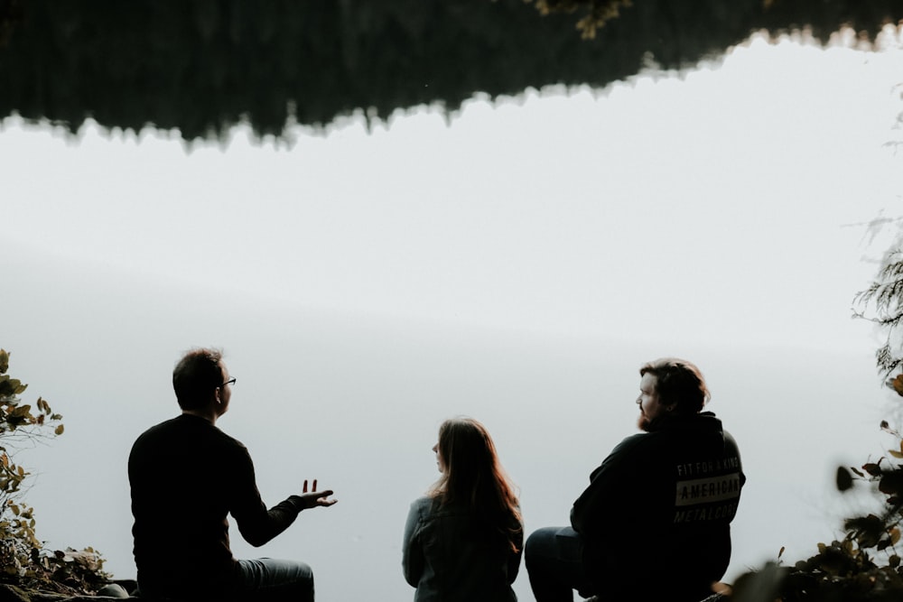 silhouette of three people sitting on cliff under foggy weather