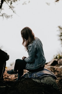 woman in blue jacket sitting on rock