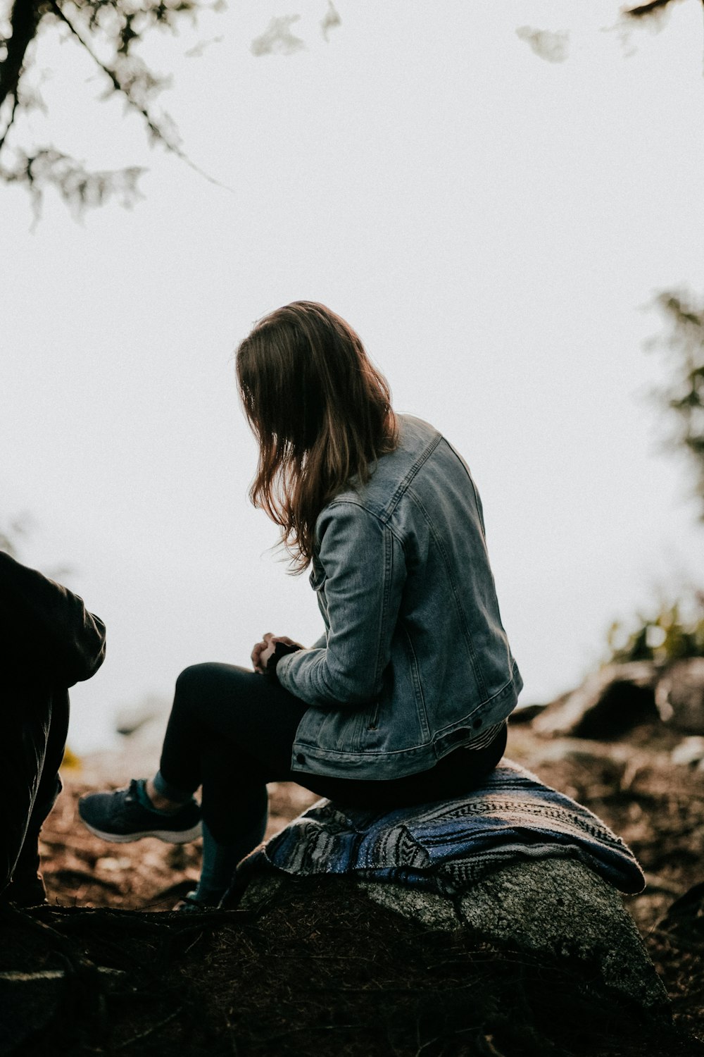 woman in blue jacket sitting on rock