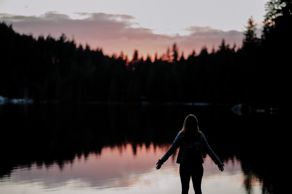 Femme debout avec les mains écartées sur le côté face au lac au coucher du soleil