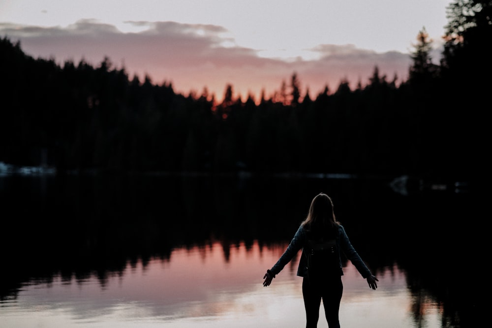 夕暮れ時に湖に面した横に両手を広げて立っている女性