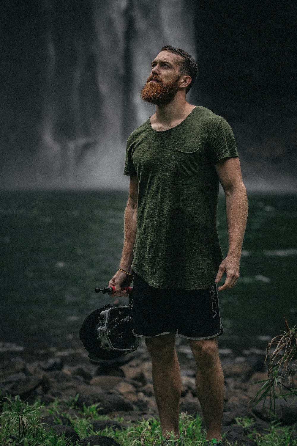 um homem com barba em pé em frente a uma cachoeira