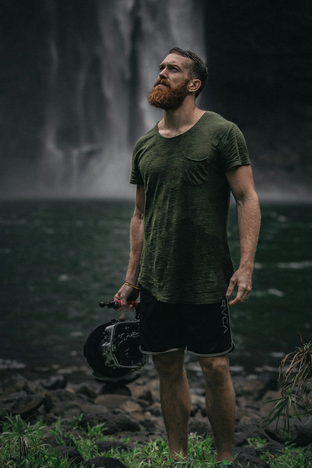 Un homme avec une barbe debout devant une cascade
