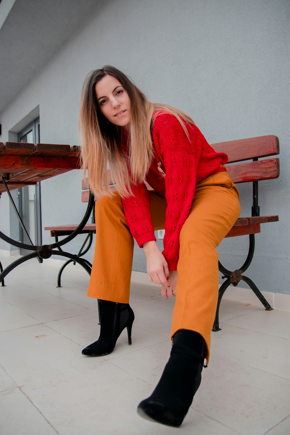 woman sitting on bench wearing red jacket and orange pants