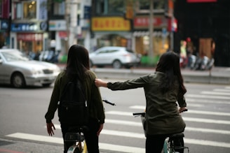 Instructor guiding a student on a two-wheeler in a calm urban setting.