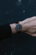 Elegant wrist wearing a slim, modern watch against a soft, neutral background.