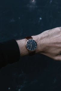 Elegant wrist wearing a slim, modern watch against a soft, neutral background.