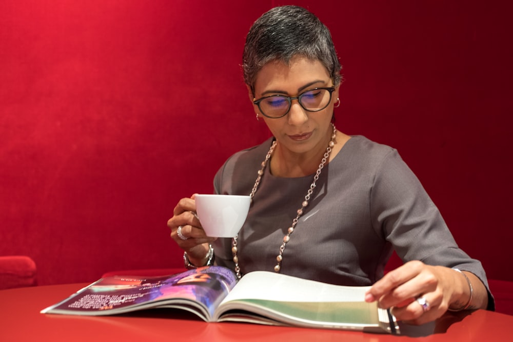 woman in grey shirt reading magazine while having coffee