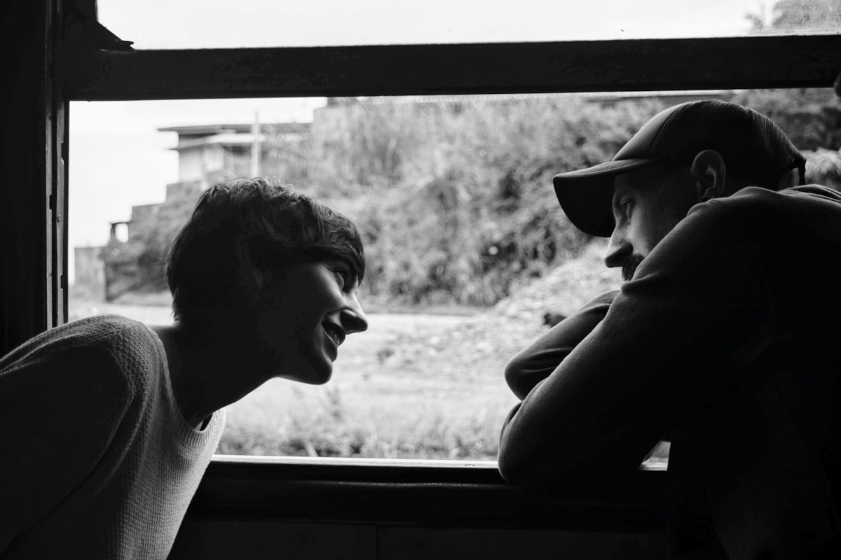 Two people facing each other across a windowsill in black and white, one mid-laugh, the other listening intently