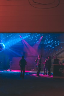 Guests dressed to impress, mingling near the bar bathed in charcoal and electric blue lighting.