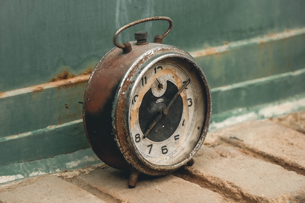 an old rusty clock sitting on the ground