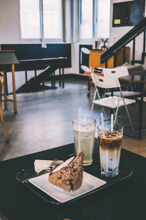 A cozy café scene featuring a steaming beverage and a slice of cake on a pastel pink surface.