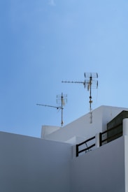 Antennas are mounted on the top of a minimalist white building against a clear blue sky. The architectural style is clean and geometric, with sharply defined edges.