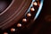 Close-up of a mechanical component with circular grooves and a row of metallic rivets. The image displays intricate details and textures, emphasizing the precision in engineering. Warm lighting highlights the metallic tones, adding depth and contrast to the scene.
