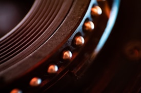 Close-up of a mechanical component with circular grooves and a row of metallic rivets. The image displays intricate details and textures, emphasizing the precision in engineering. Warm lighting highlights the metallic tones, adding depth and contrast to the scene.