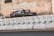 A row of campaign posters is prominently displayed on a concrete barrier, featuring a man's face with text in a non-English script. Behind the barrier, two cars are parked against a weathered wall with peeling paint.
