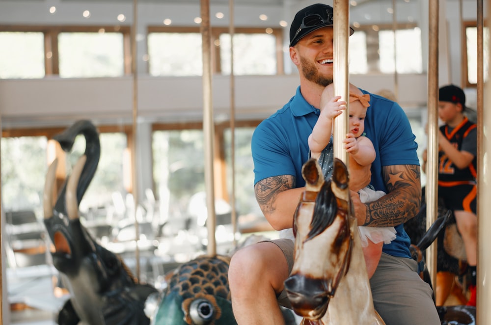 man riding horse carousel with baby