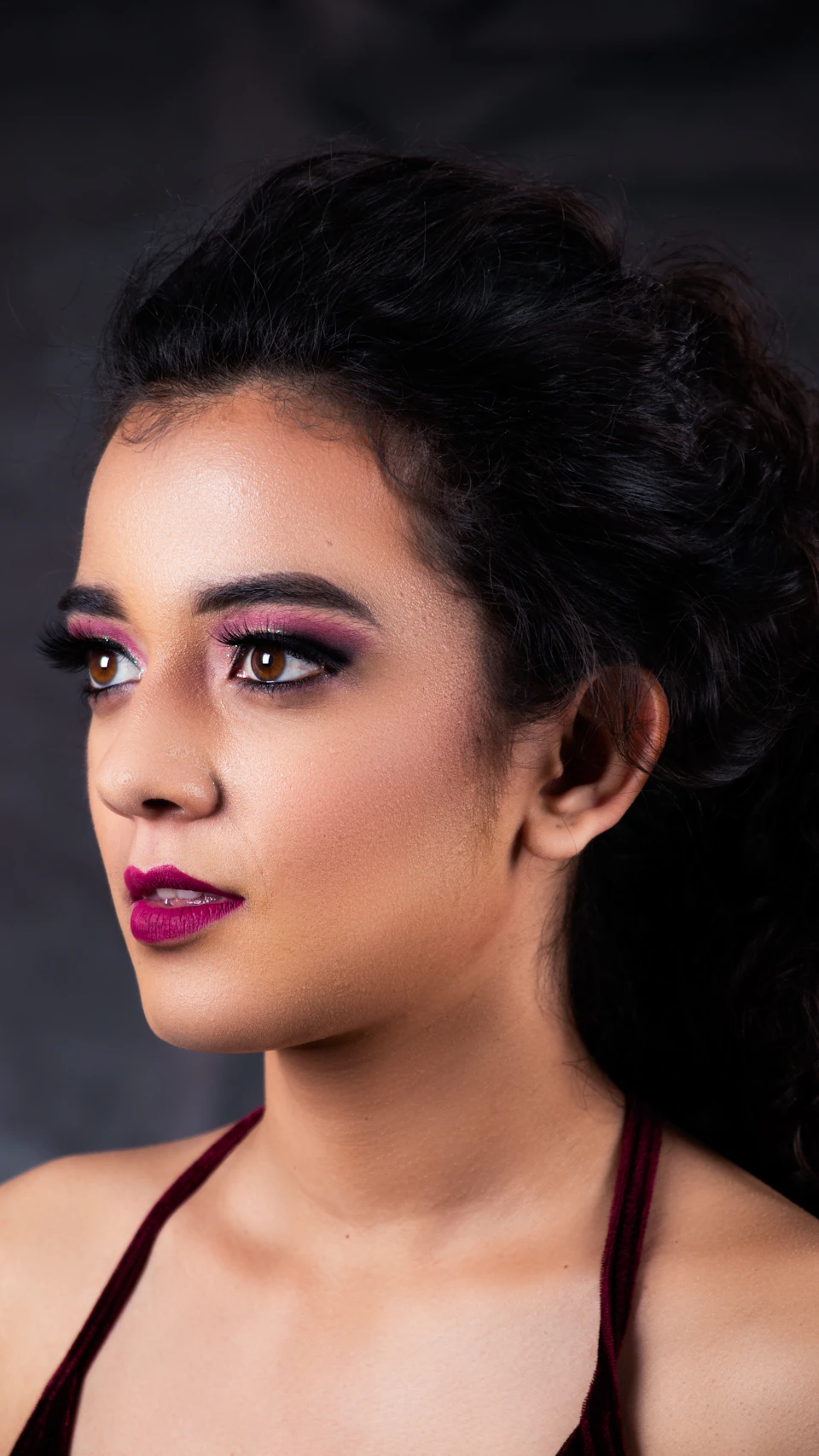 Young woman with dark hair, red dress, and burgundy top, gazing out of frame