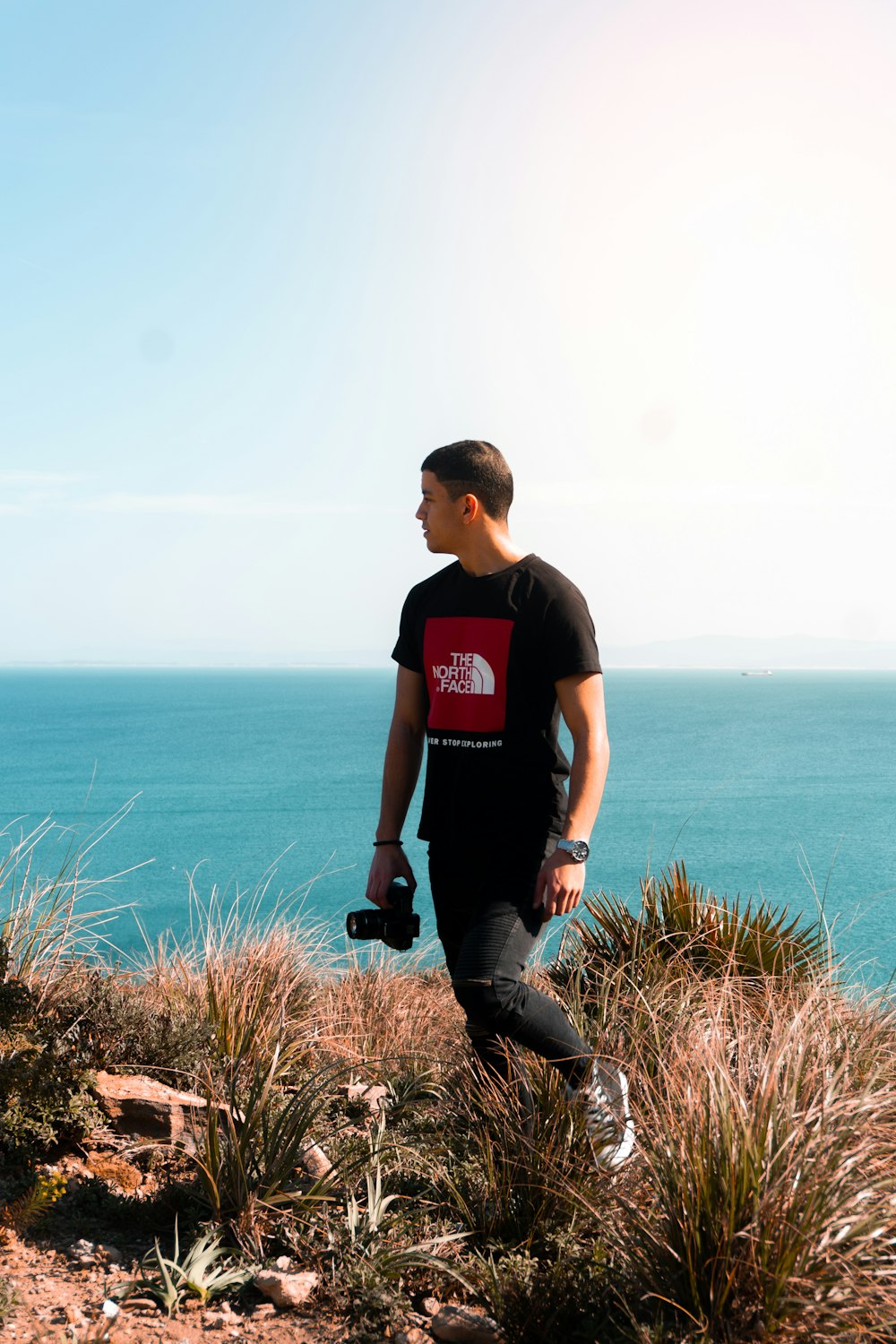 man in black crew neck t-shirt and black pants sitting on brown rock near body