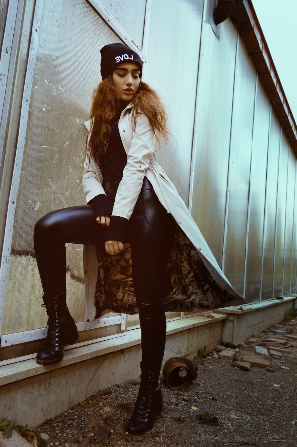 woman in white coat and black leggings standing beside wall