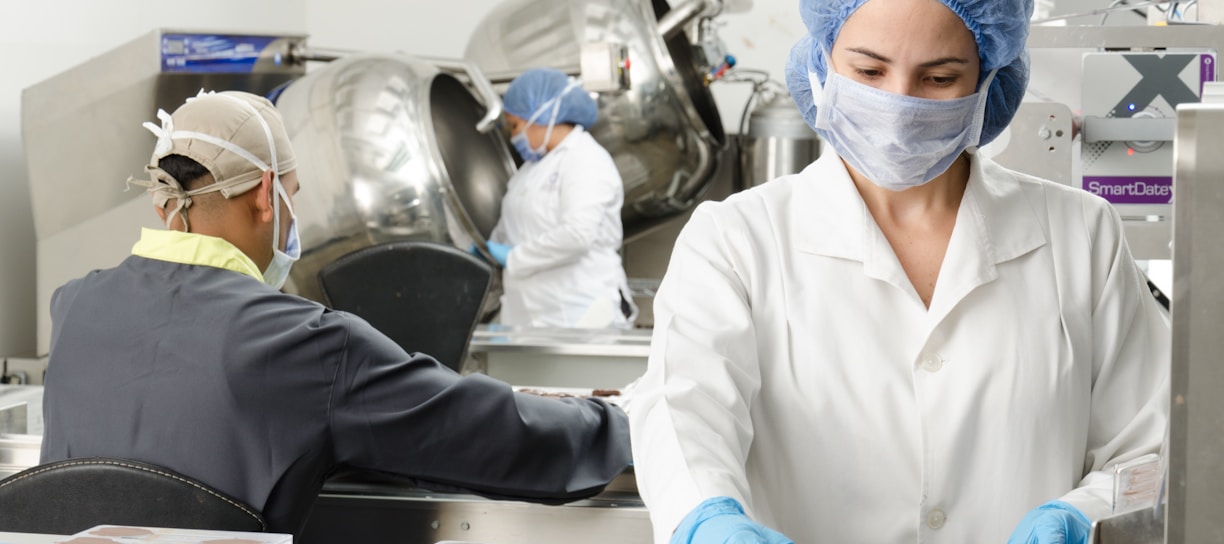 three people inside factory wearing masks and coats