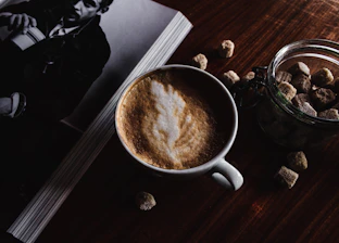 A grainy black-and-white photo of a dimly lit café corner with an open book and a steaming cup of coffee at 2am.