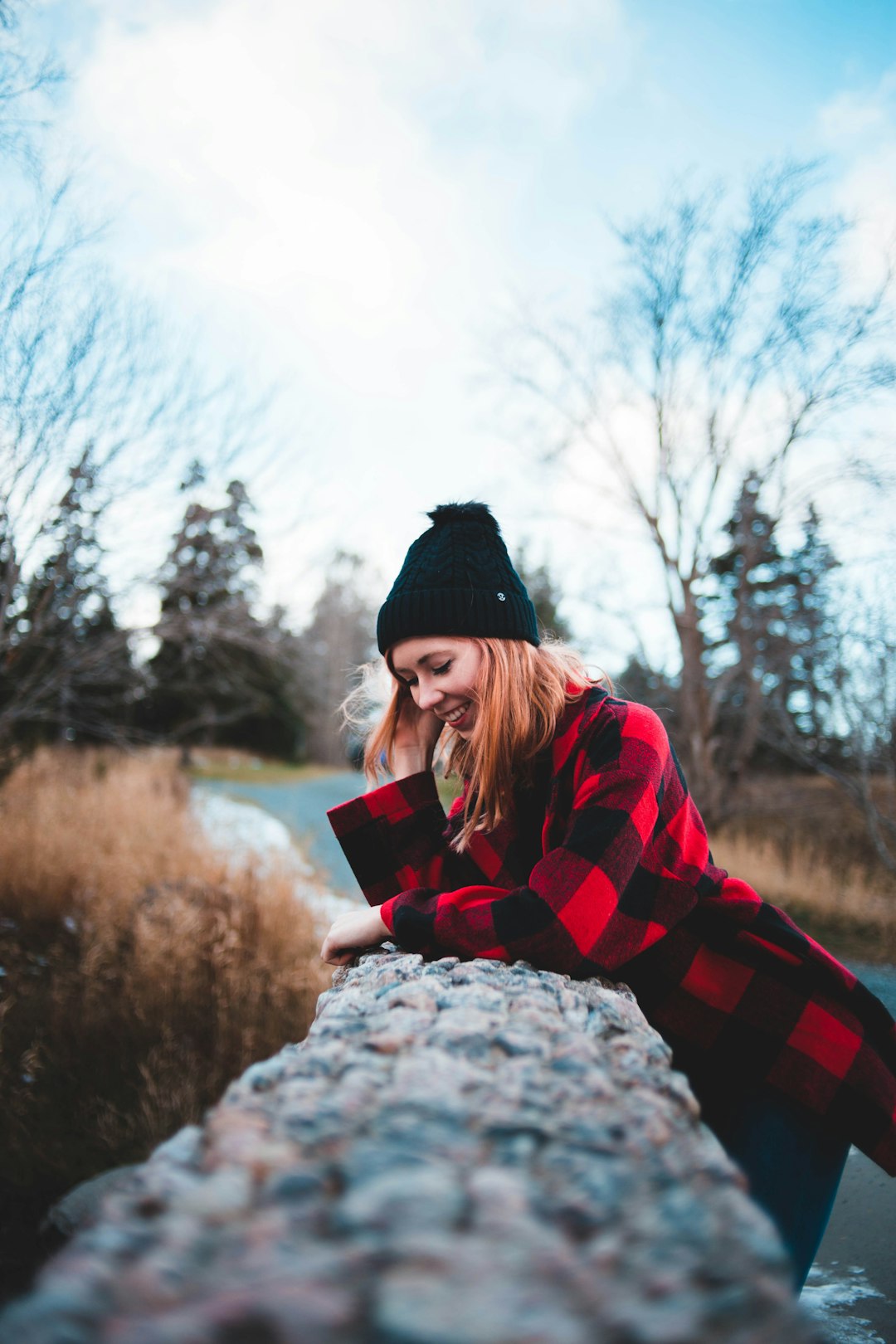 smiling woman learning on concrete barricade beside road during daytime