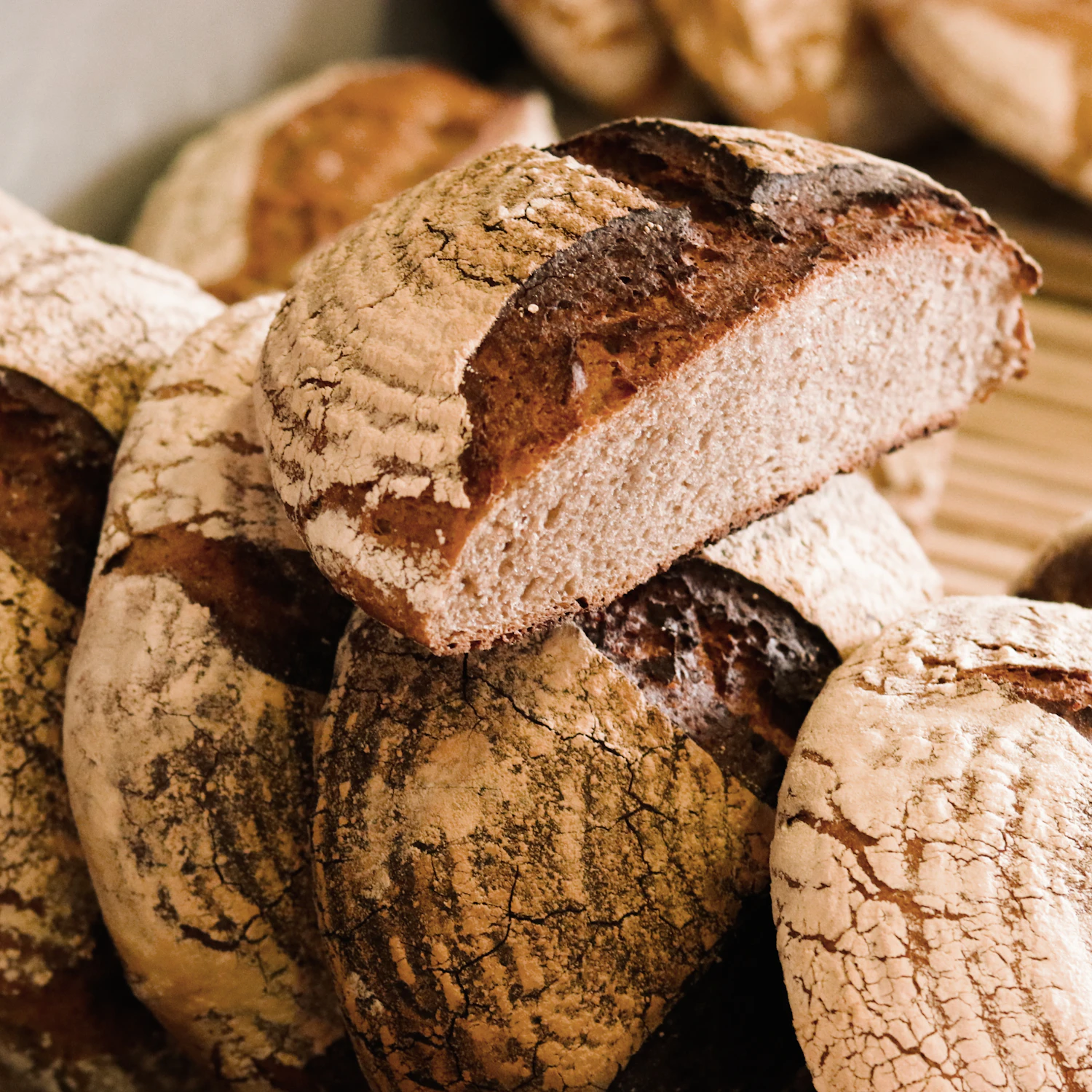 A stack of dark round loaves tipped against each other, one cut through to show the crumb